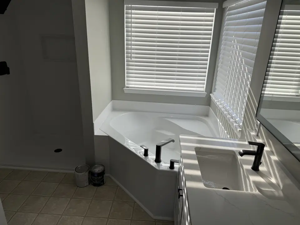 Corner soaking tub set under a window with a matte black deck-mount filler