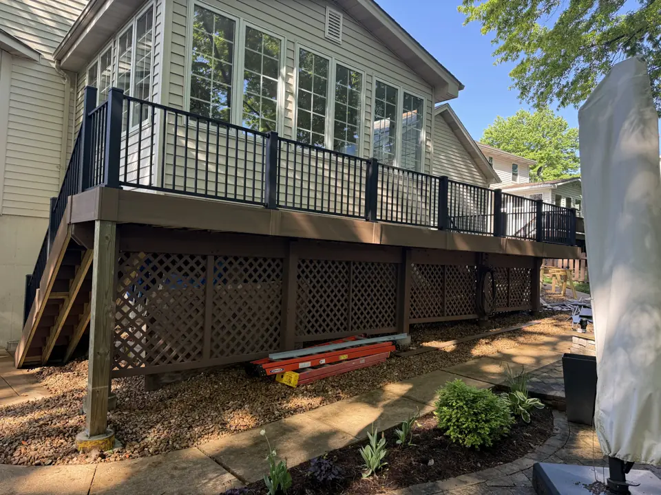 Raised composite deck with black aluminum railing and a stained lattice skirt on the back of a two-story house