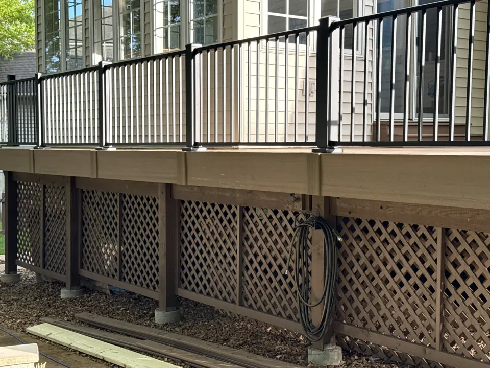 Close view of a black aluminum picket railing on a composite deck with a stained wood lattice below