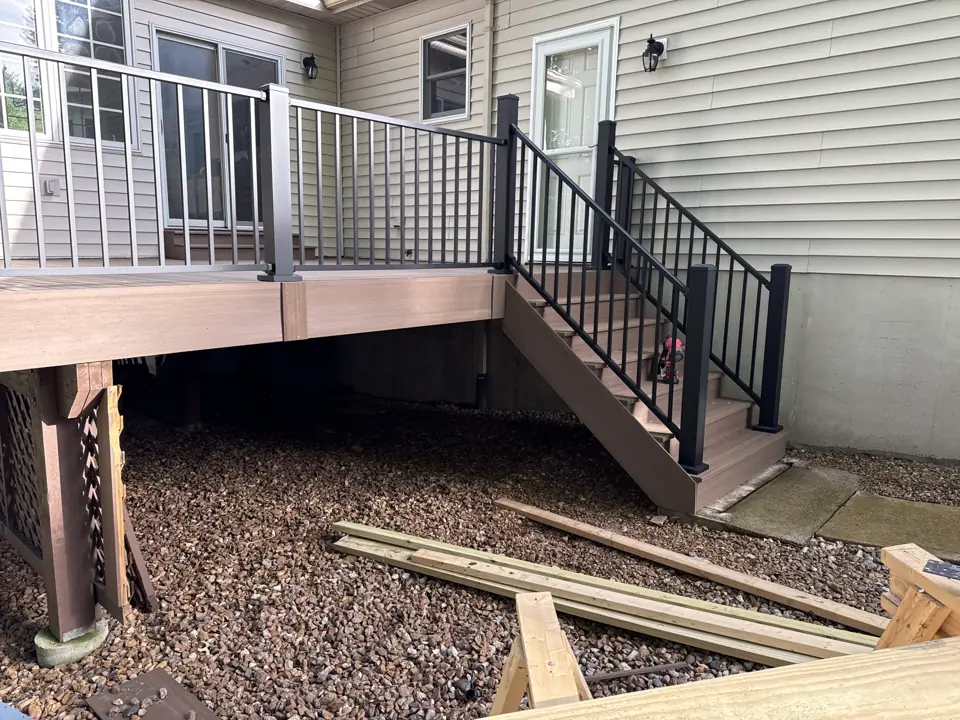 Deck stair landing with black aluminum railing meeting the house wall, gravel bed and new posts below