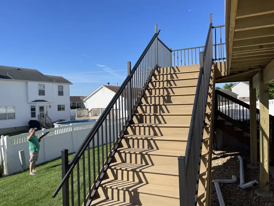 New composite deck stair with black aluminum railing descending to a lawn, seen from the deck above