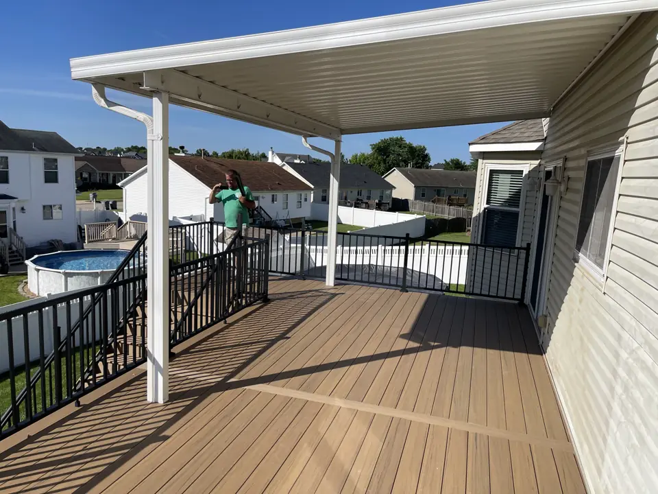 Composite deck with a white aluminum roof cover over the section by the house, black railing and a view of the neighborhood