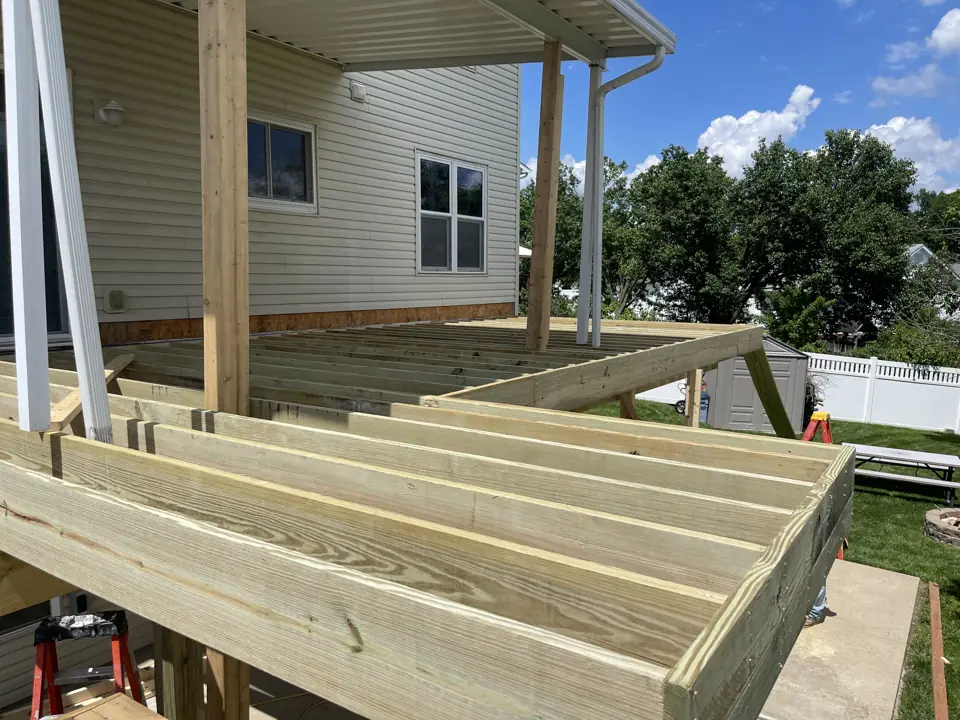 Deck framing with pressure-treated joists and hangers on a second-story deck, roof cover posts in place