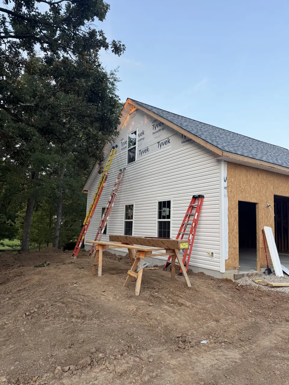 Gable end of a new detached garage in white vinyl siding on a wooded lot
