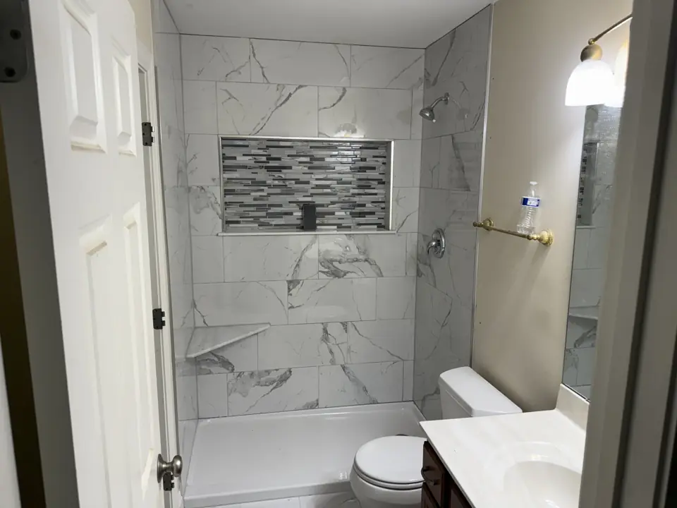 Small hall bathroom with a marble-look tiled tub surround and a horizontal glass mosaic band through the shampoo niche