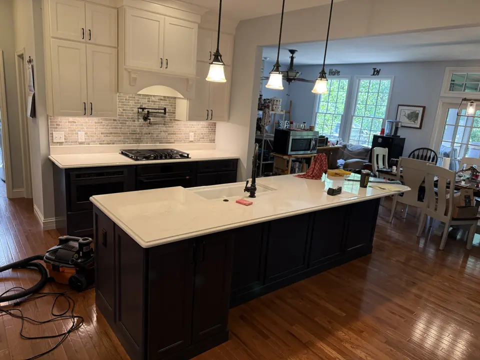 Kitchen with cream perimeter cabinets, white subway tile, a dark espresso island with pendant lights and hardwood floor into the dining room