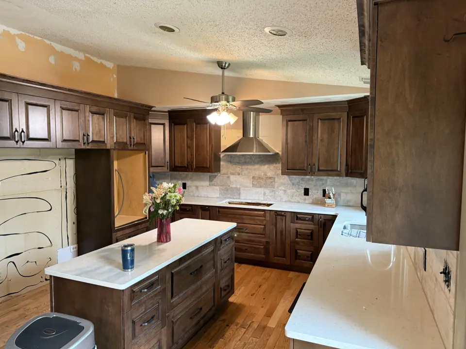 Kitchen with dark stained cabinets, white quartz island and counters and a travertine backsplash, walls prepped for paint