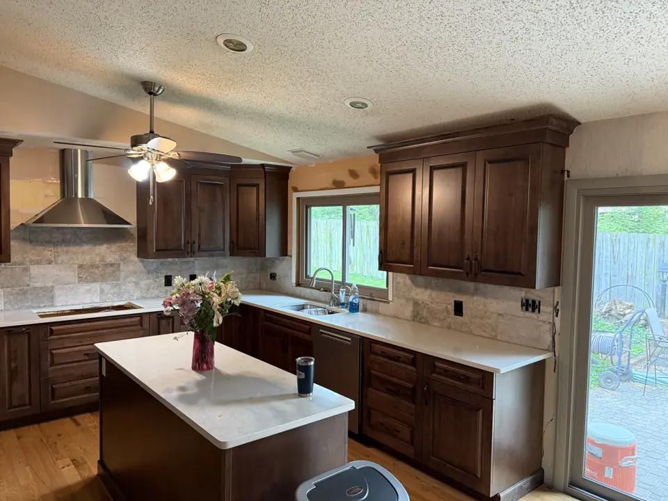 Stained cabinet kitchen with new stainless range hood, white quartz counters and a ceiling fan, light wood floor