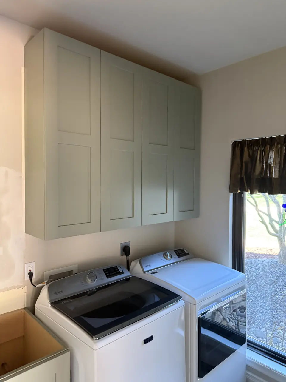 Laundry room with sage green upper cabinets over a top-load washer and dryer, window with a small valance