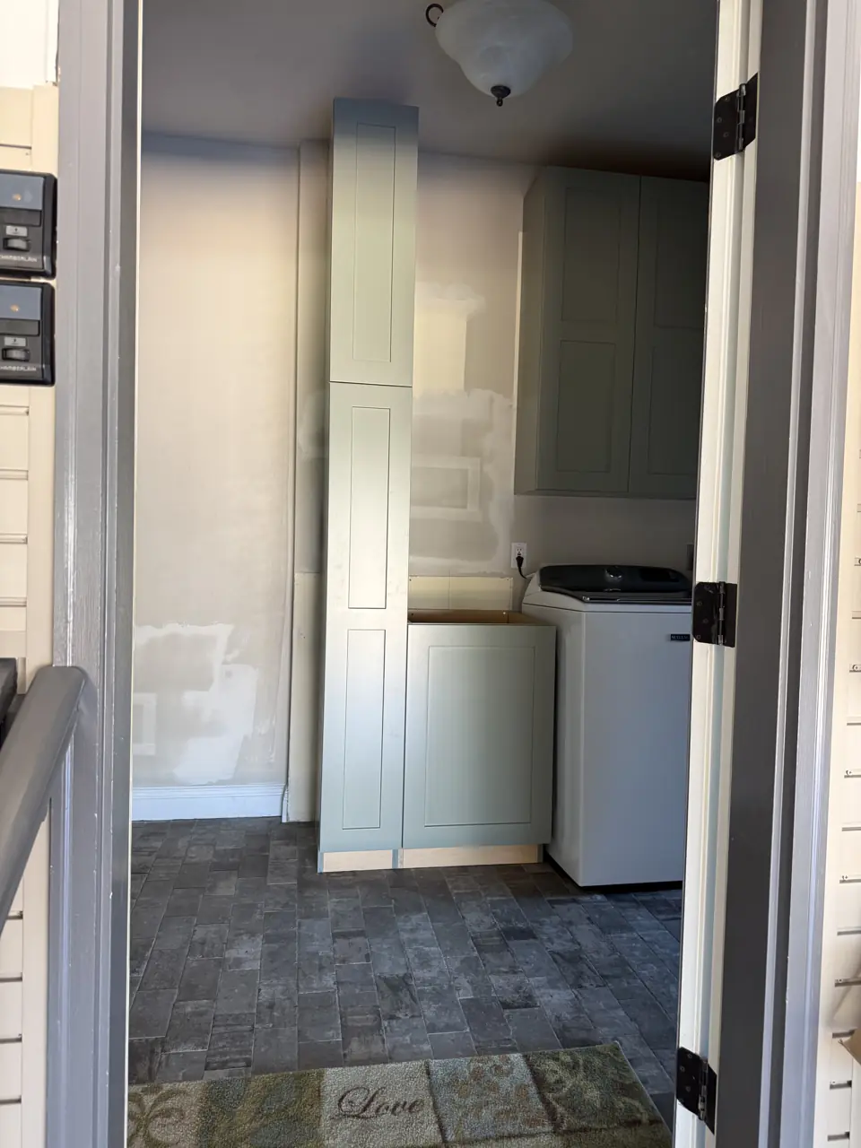 View through a doorway into a laundry room with tall sage cabinets and a stone checkerboard floor