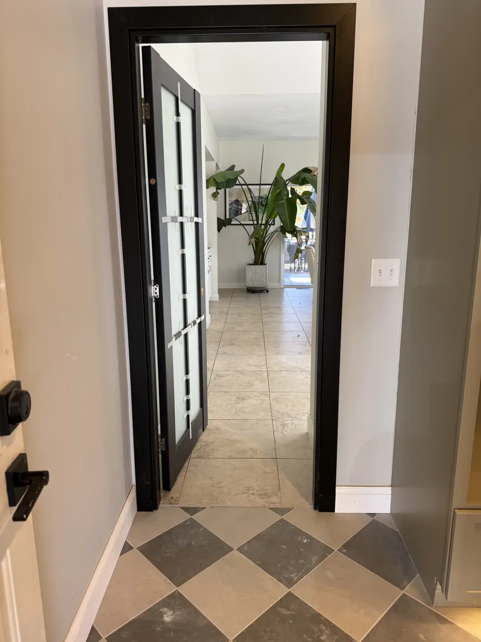 Black-framed French door opening from a checkerboard-tiled mudroom into a bright living area