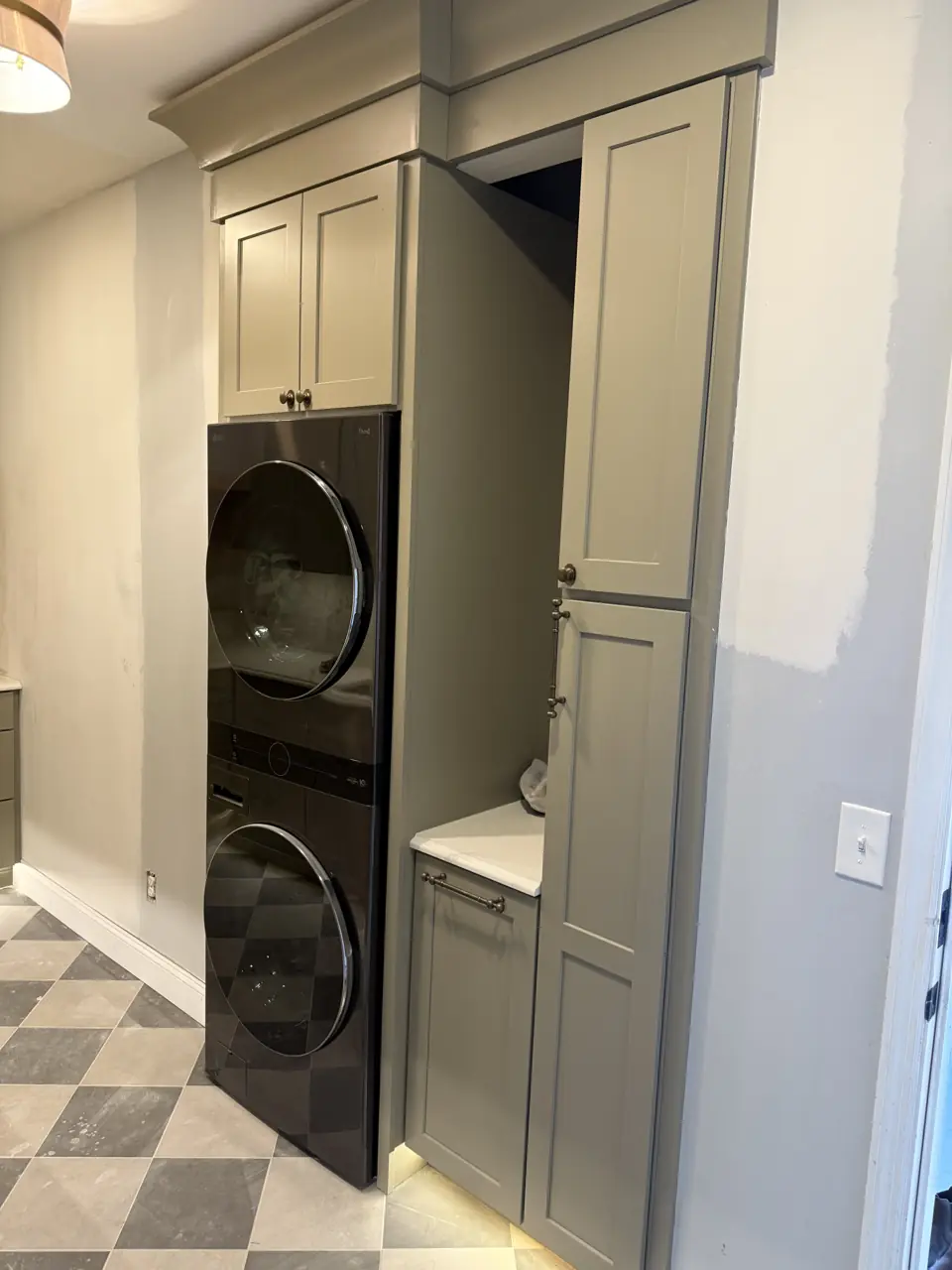 Stacked washer and dryer built into a full-height sage cabinet bay with storage above