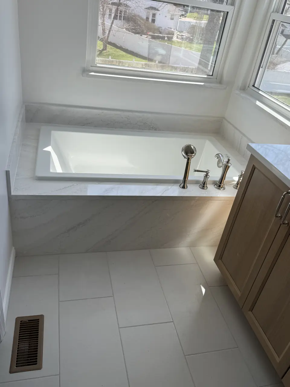 Deck-mounted tub with polished chrome filler, porcelain tile floor and oak vanity, window overlooking the yard
