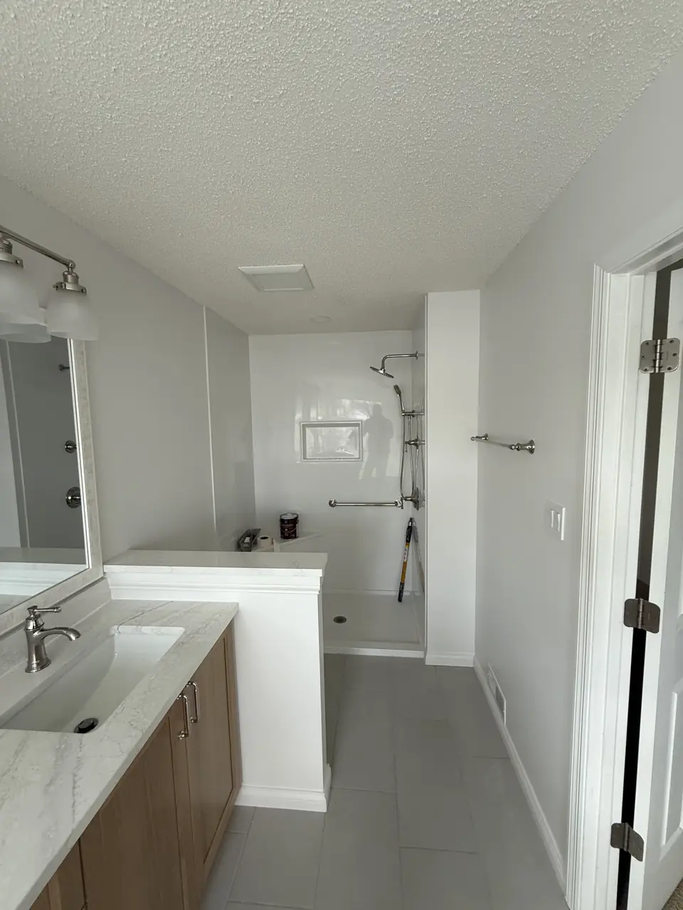 Bathroom with a long oak double vanity, white counter and a walk-in shower with a linear niche at the far end