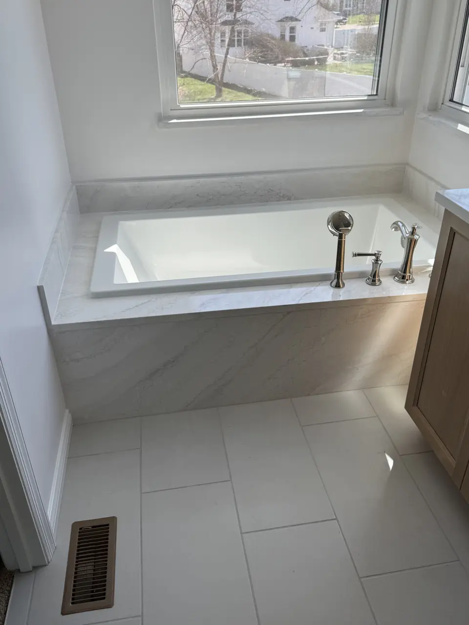 Drop-in tub with chrome deck-mount filler, porcelain surround and oak vanity, seen from the bathroom door