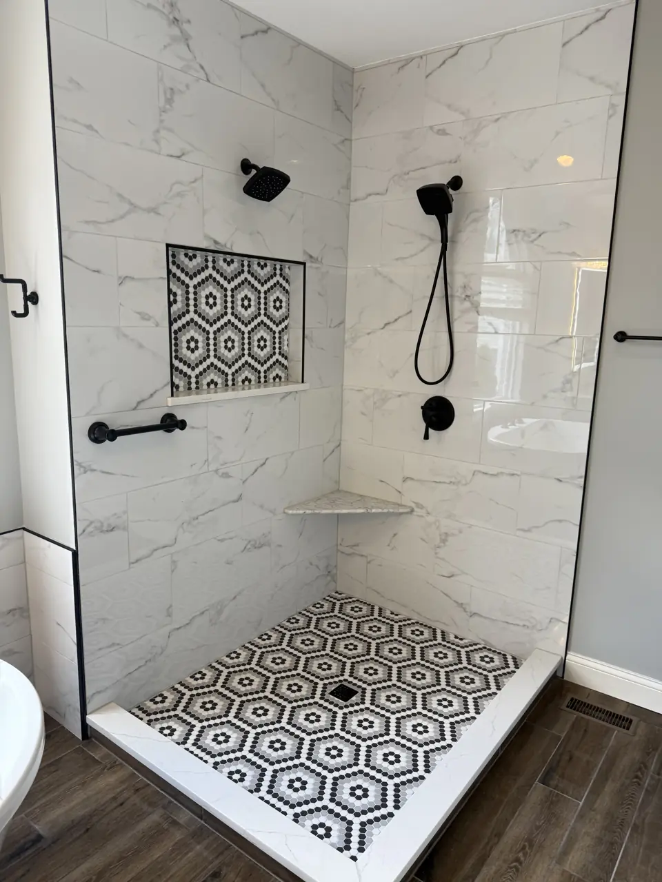 Walk-in shower with marble-look wall tile, a patterned black and white hexagon mosaic floor and matte black fixtures