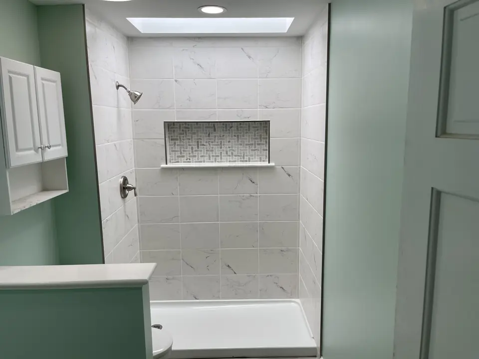 Tiled shower with a low threshold base, marble-look subway tile, framed niche and a short knee wall, in a sage green bathroom