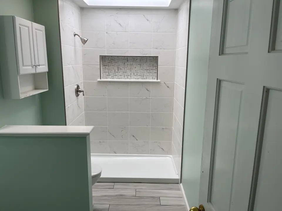 Tub-to-shower conversion with tiled walls and niche, seen past a white medicine cabinet and the bathroom door