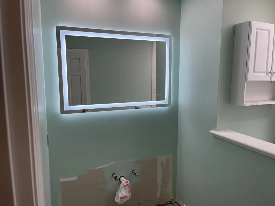 Sage green bathroom with a lit rectangular mirror, wood-look plank tile floor and a white wall cabinet