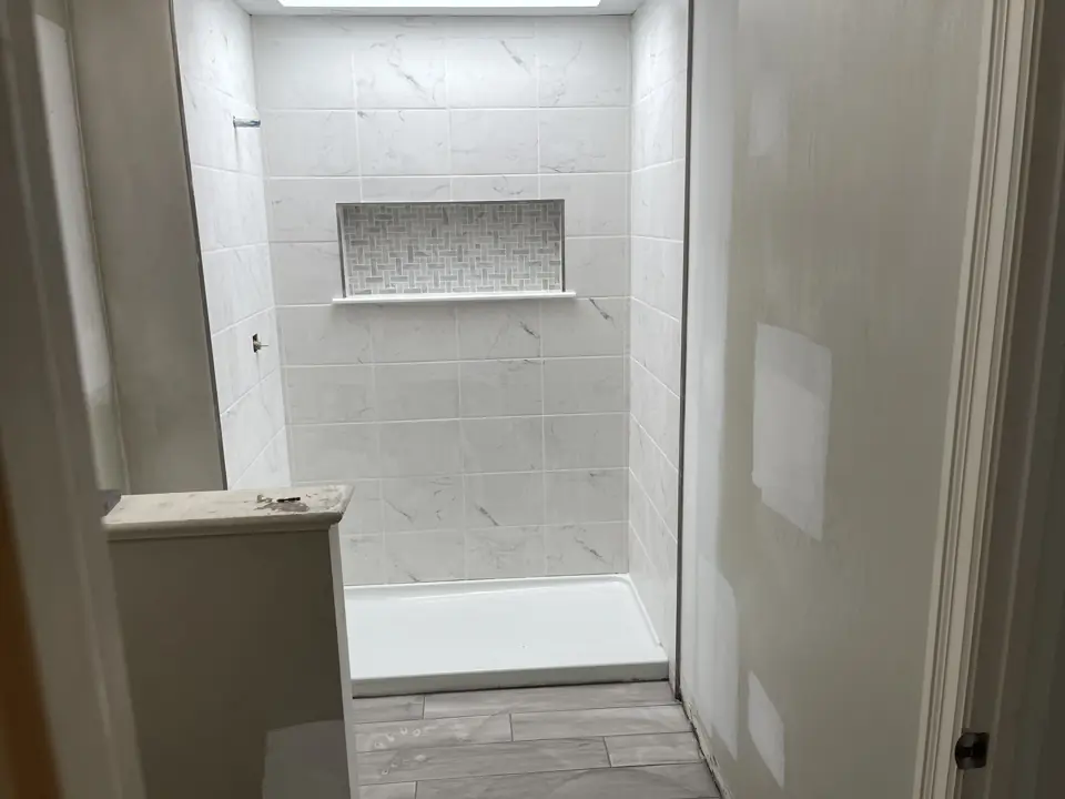 Close view of a low-threshold shower base with marble-look subway tile walls and a darker mosaic niche