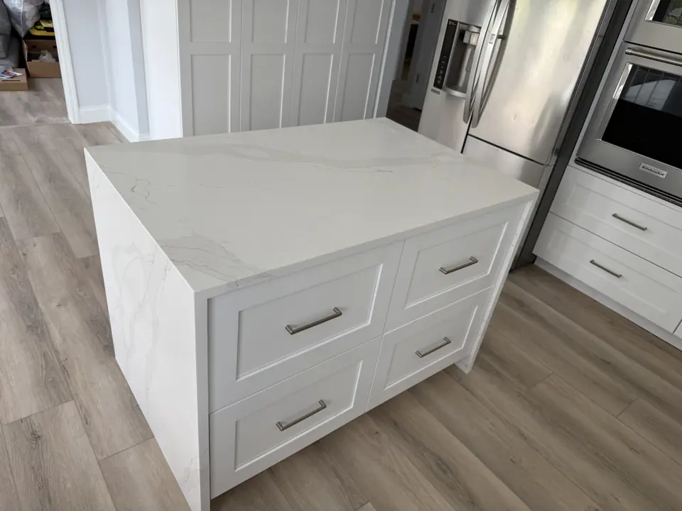Close view of a quartz waterfall island end with grey veining continuing down the side, over light plank flooring