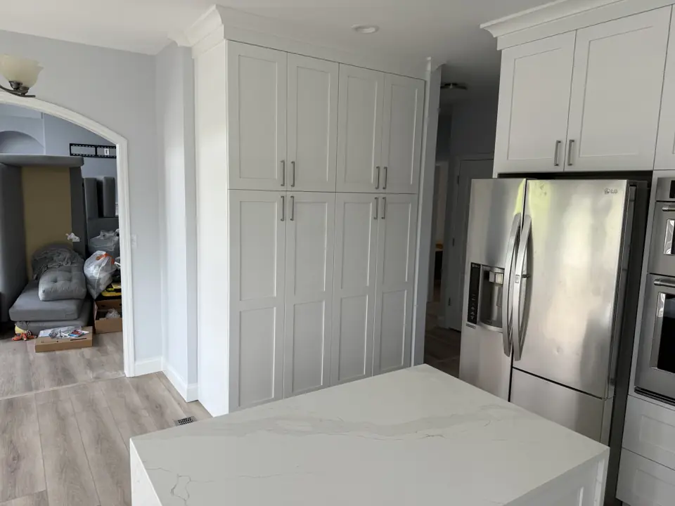 Floor-to-ceiling white cabinetry with stacked crown molding and a stainless refrigerator, seen across the island
