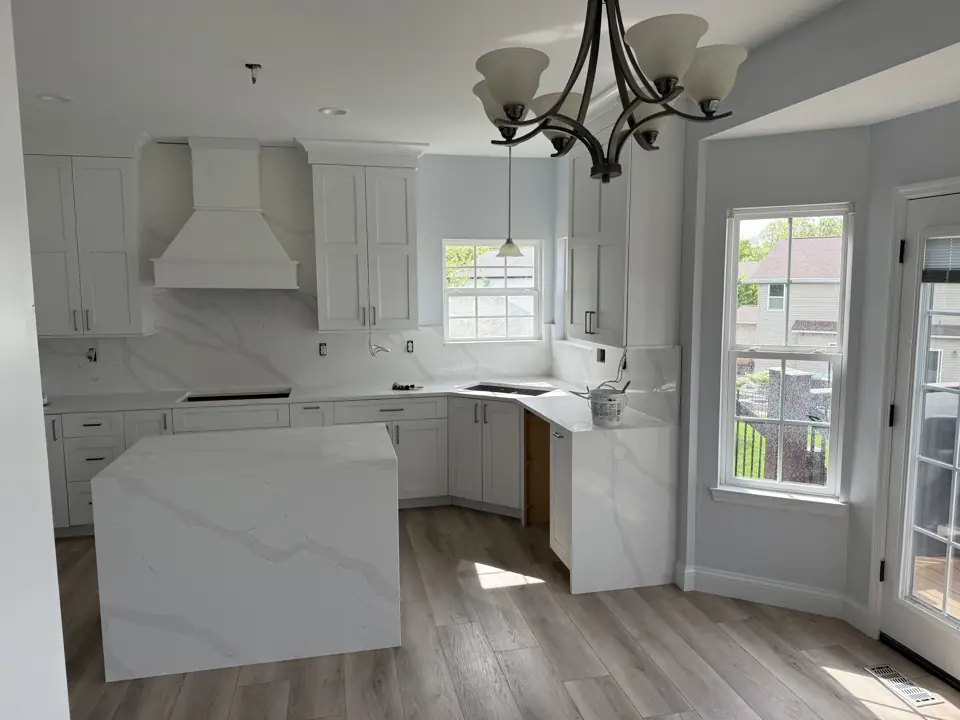 Finished white kitchen with a custom painted hood, bay window over the sink and a chandelier over the island